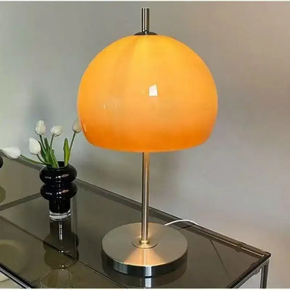 Orange table lamp with a black base on a reflective surface.